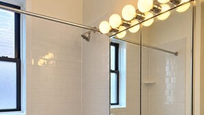 Une salle de bain moderne avec une baignoire blanche, un lavabo sur colonne et un grand miroir avec des lumières au-dessus.