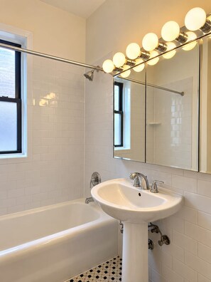 Ein modernes Badezimmer mit einer weißen Badewanne, einem Standwaschbecken und einem großen Spiegel mit Beleuchtung darüber.