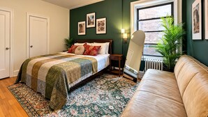 Une chambre à coucher avec un lit, une table de chevet, un miroir, une fenêtre et un mur vert.