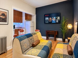 A living room with a sofa, a television displaying Netflix content, a small table, and a potted plant.