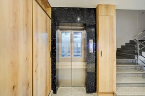 An elevator with a glass door, a wooden wall, and a staircase with metal railings. - Super Townhouse Oak Banaras Central (Varanasi)