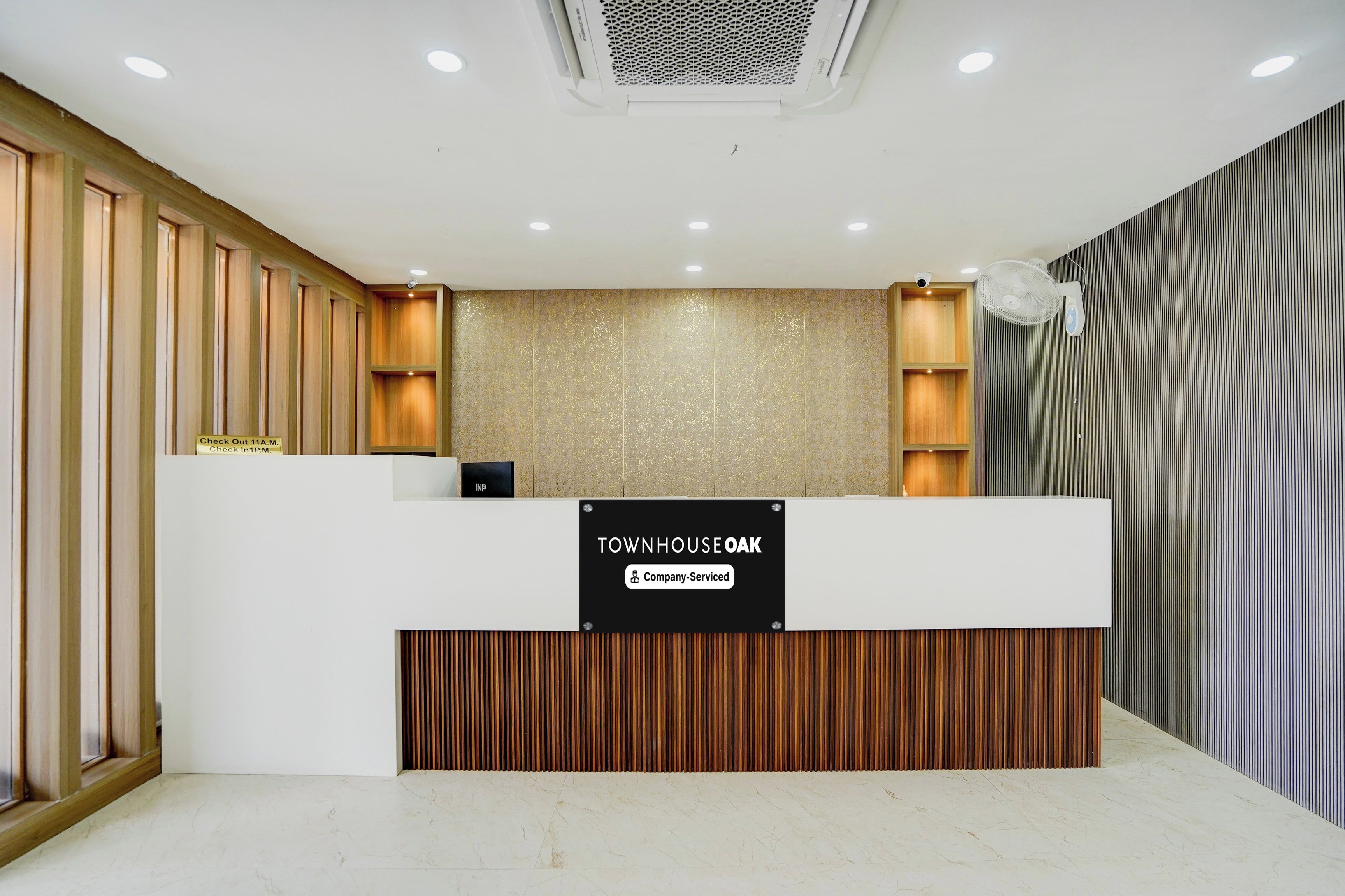 A reception desk with a sign indicating it's company-serviced, wooden paneling on the walls, and a marble floor.