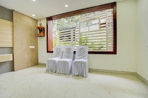 Una habitación con un separador de madera, un ventanal con vistas a la vegetación y dos sillas cubiertas con telas blancas.
