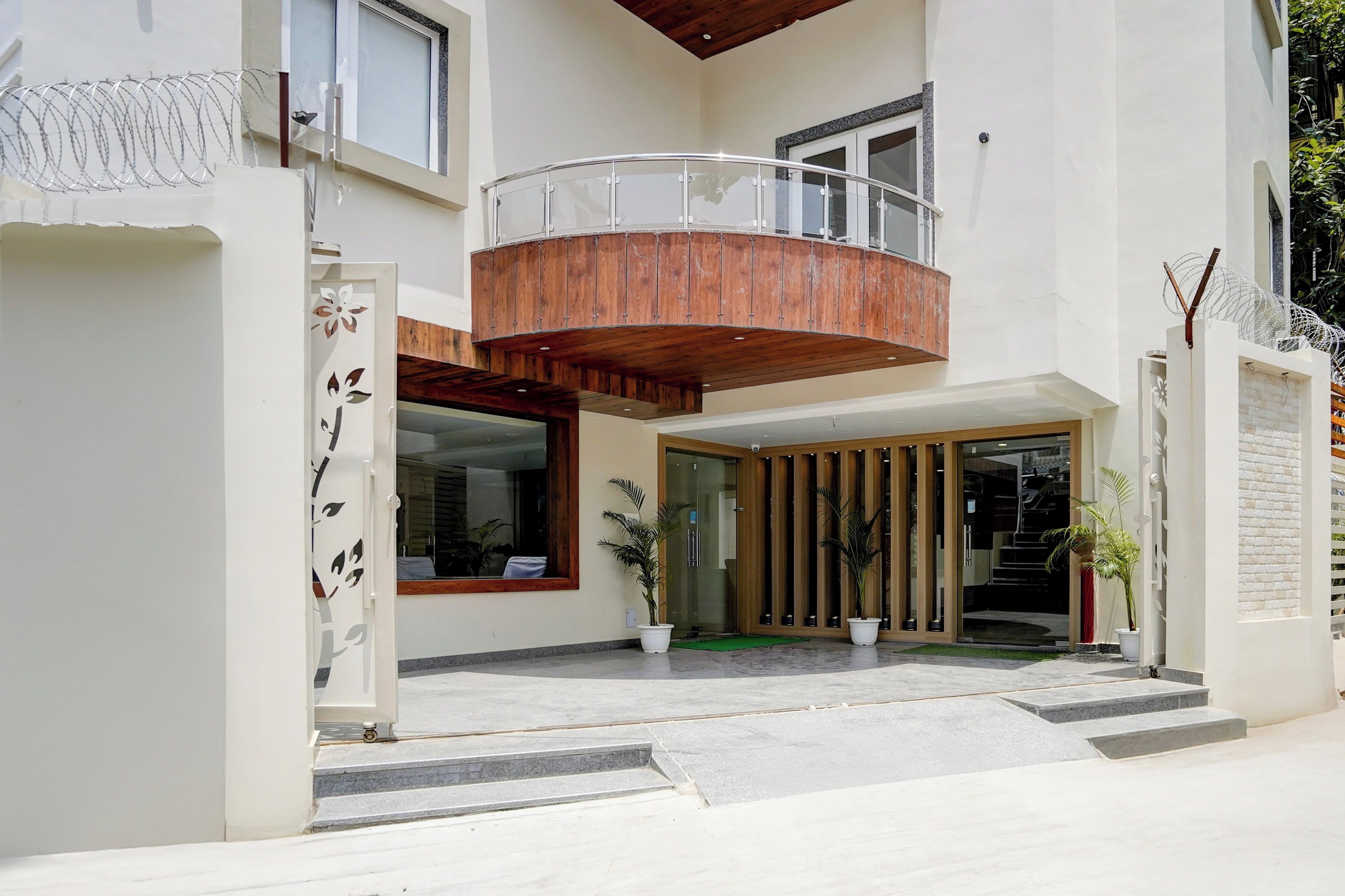 A modern two-story building with a balcony, a glass entrance, and potted plants.