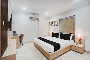 A hotel room with a bed, bedside table, desk, chair, and an air conditioning unit. - Super Townhouse Oak Banaras Central (Varanasi)