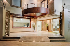 A modern interior with a wooden staircase, a large mirror, and a reception area with a plant. - Super Townhouse Oak Banaras Central (Varanasi)