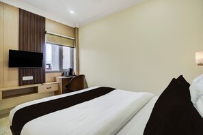 Habitación de hotel con cama, escritorio, silla, televisor y ventana.