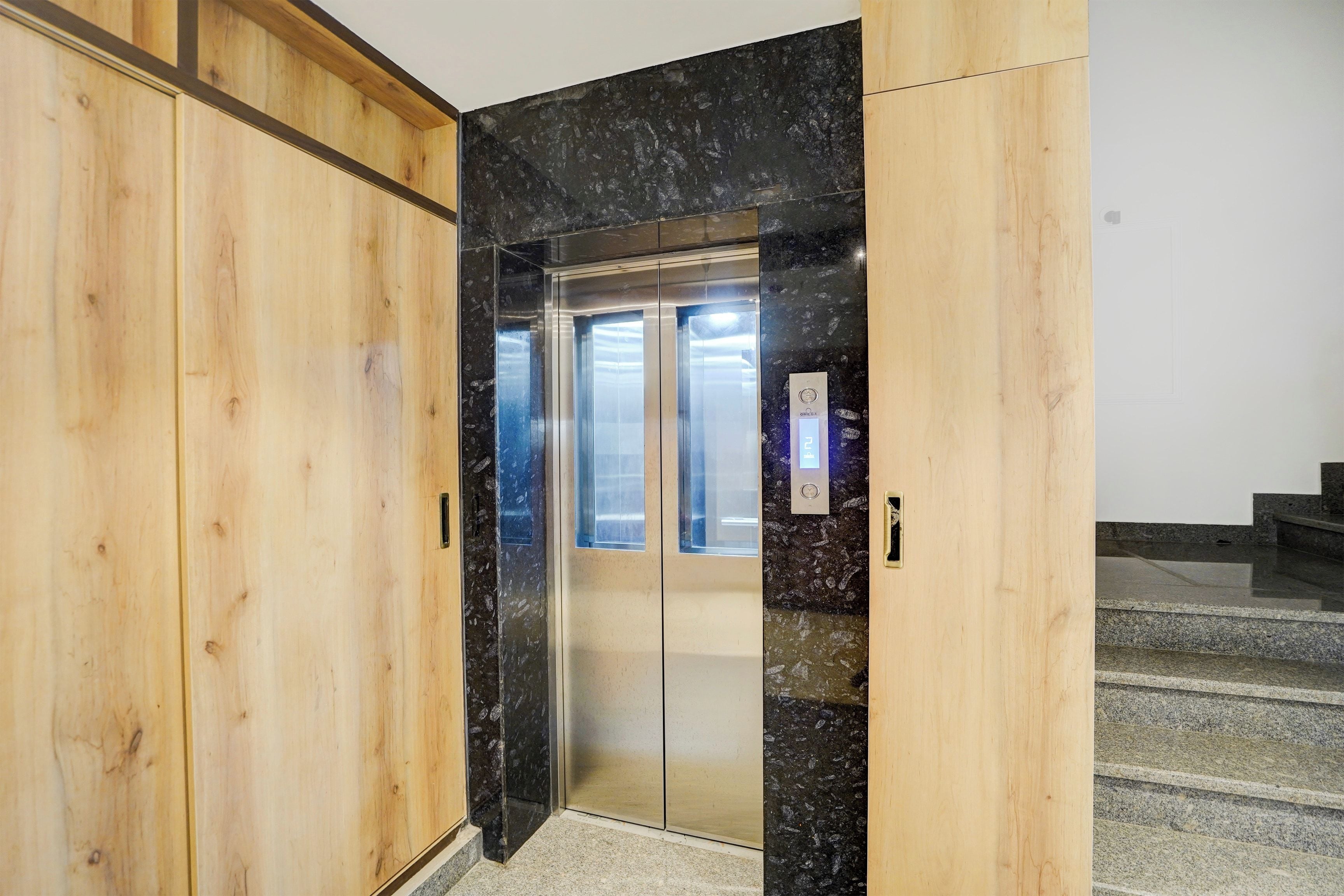 An elevator with a wooden door frame and a marble wall.