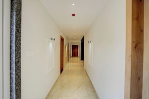 A corridor with doors on both sides, a marble floor, and recessed lighting on the ceiling. - Super Townhouse Oak Banaras Central (Varanasi)