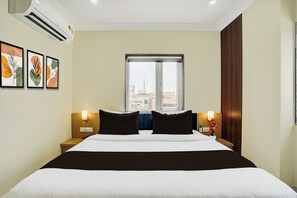 A hotel room with a bed, bedside tables, a window, and wall-mounted air conditioning. - Super Townhouse Oak Banaras Central (Varanasi)