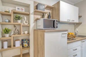 Une cuisine moderne avec des meubles blancs, un four à micro-ondes et des étagères en bois où sont rangés divers ustensiles de cuisine.