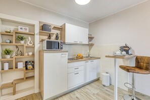 A modern kitchen with white cabinetry, a microwave, and a sink. There are wooden shelves with decorative items and a small dining area with a chair. - Wonderful pet-friendly 2-bedroom apartment with AC in quaint Pazin (Pazin)