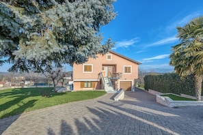 A two-story house with a paved driveway, a small front garden, and a large tree in the foreground. - Wonderful pet-friendly 2-bedroom apartment with AC in quaint Pazin (Pazin)