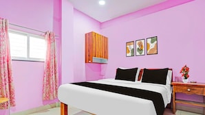 A bedroom with a bed, a nightstand, a wooden wardrobe, a window with curtains, and wall art. - Collection O Dighori Nagpur (Nagpur)