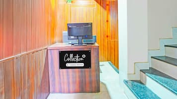 Un mostrador de recepción con un cartel que indica servicio de empresa, un televisor y una escalera a la derecha.