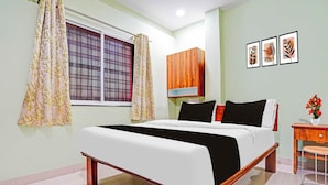 A bedroom with a bed, a nightstand, a wooden wardrobe, a window with curtains, and wall art. - Collection O Dighori Nagpur (Nagpur)