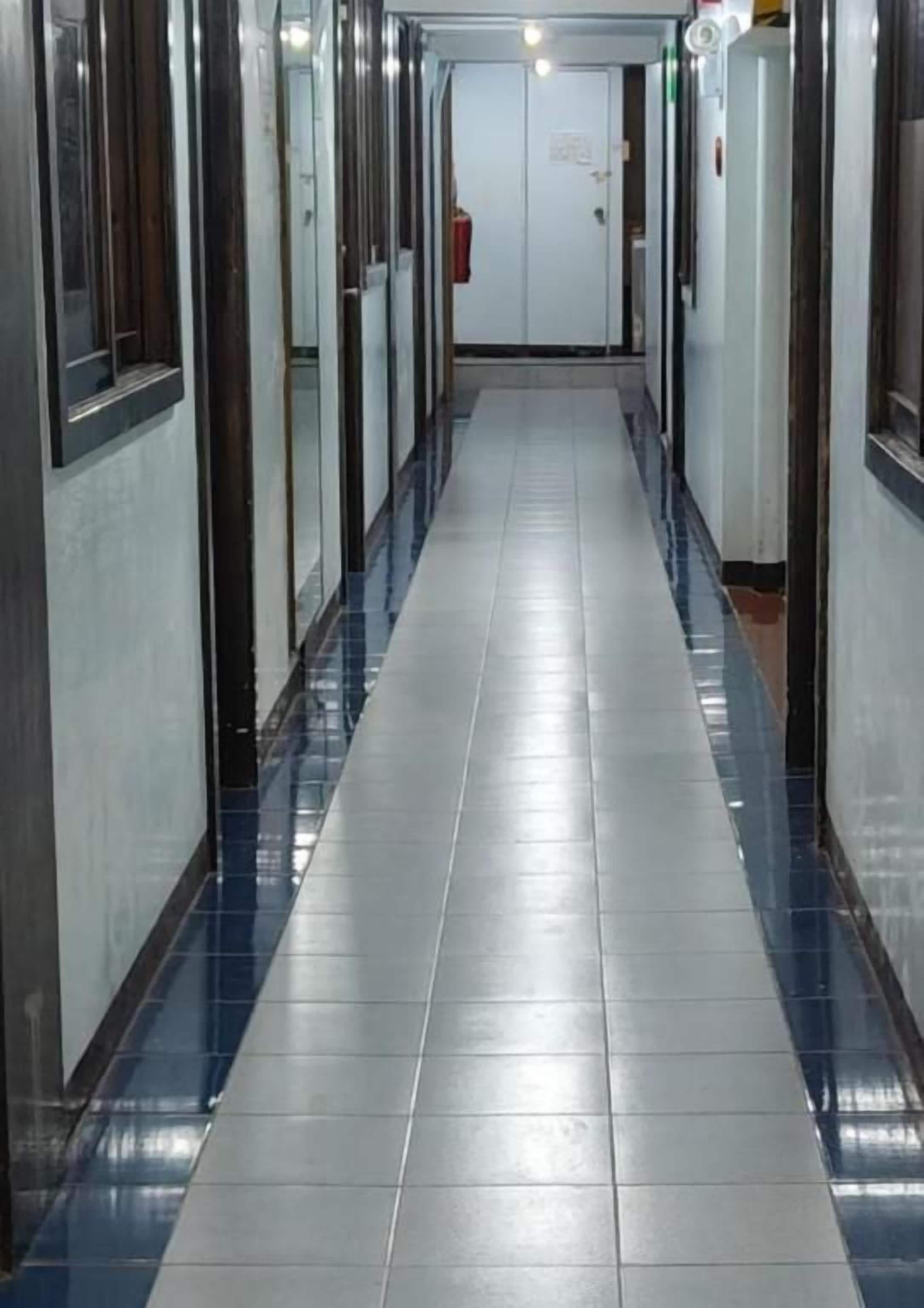 Un pasillo con piso de baldosas, puertas a ambos lados y un extintor de incendios fijado en la pared.
