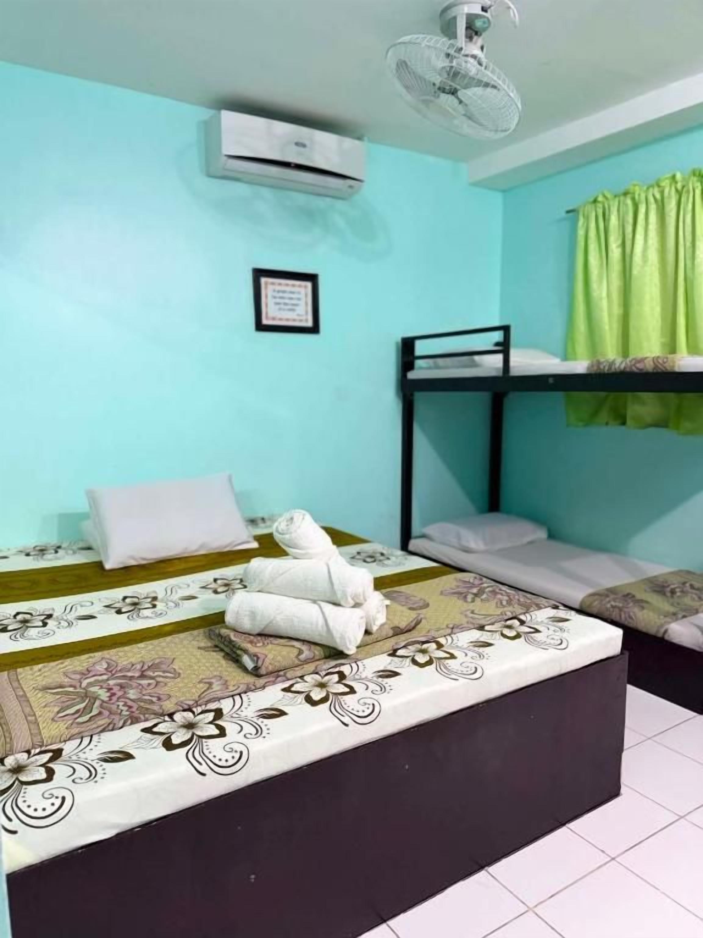 Una habitación con literas, una cama individual con ropa de cama floral, un ventilador de techo, un equipo de aire acondicionado y una cortina verde.