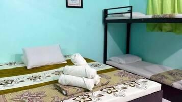 Una habitación con literas, una cama individual con ropa de cama floral, un ventilador de techo, un equipo de aire acondicionado y una cortina verde.