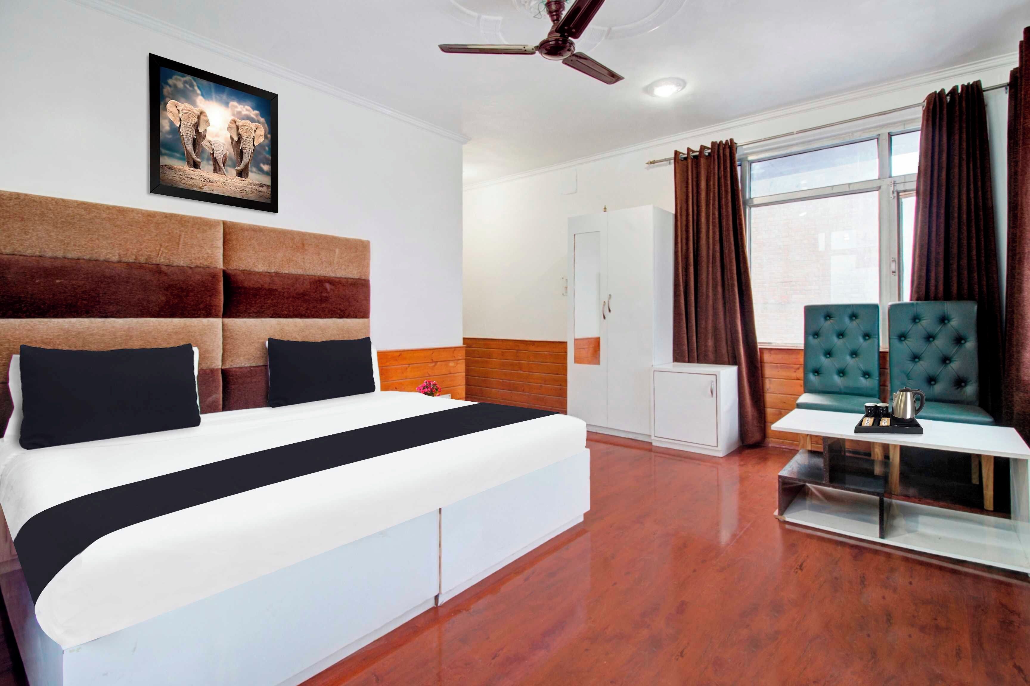 A hotel room with a large bed, a ceiling fan, a window with curtains, and a painting on the wall.