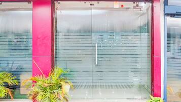 A building entrance with a glass door, a red wall, and potted plants.