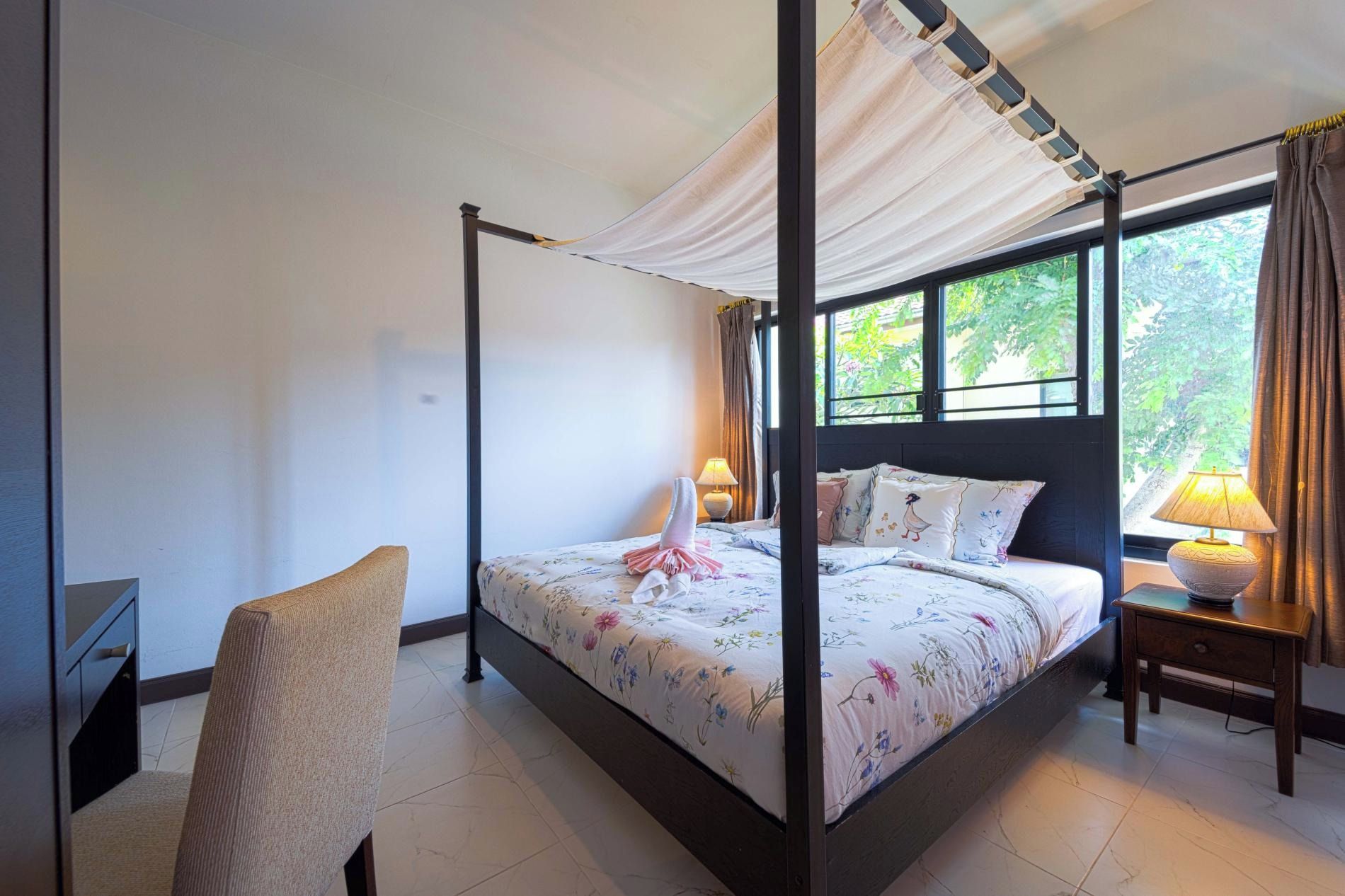 Uma cama de dossel com cortina, uma mesa de cabeceira com abajur e uma cadeira.