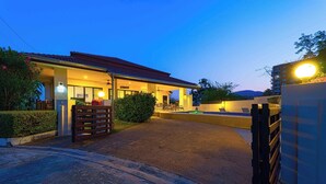 L’entrée d’un hôtel avec un espace extérieur abrité aménagé en coin salon, une piscine et une allée d’accès fermée par un portail.