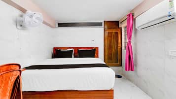 A hotel room with a bed, a wooden headboard, a white wall, a wooden door, and an air conditioning unit.