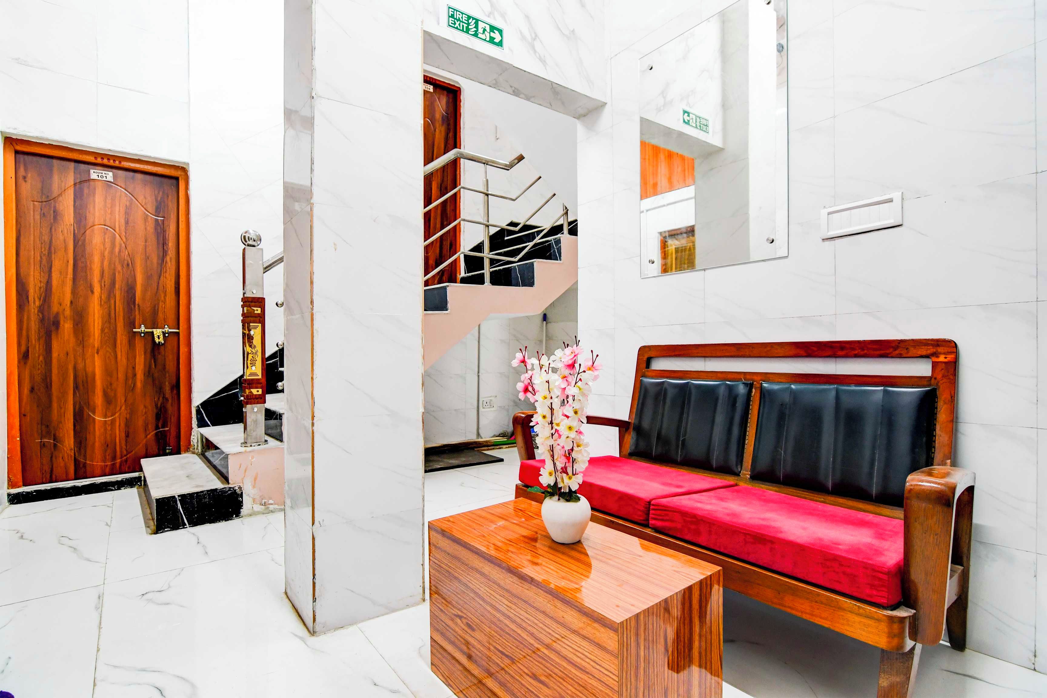 A hotel lobby with a wooden door labeled '101', a staircase, a sofa with red cushions, and a small table with a vase.