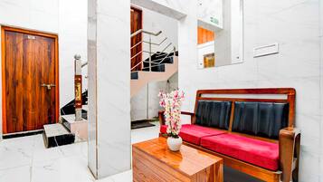 A hotel lobby with a wooden door labeled '101', a staircase, a sofa with red cushions, and a small table with a vase.