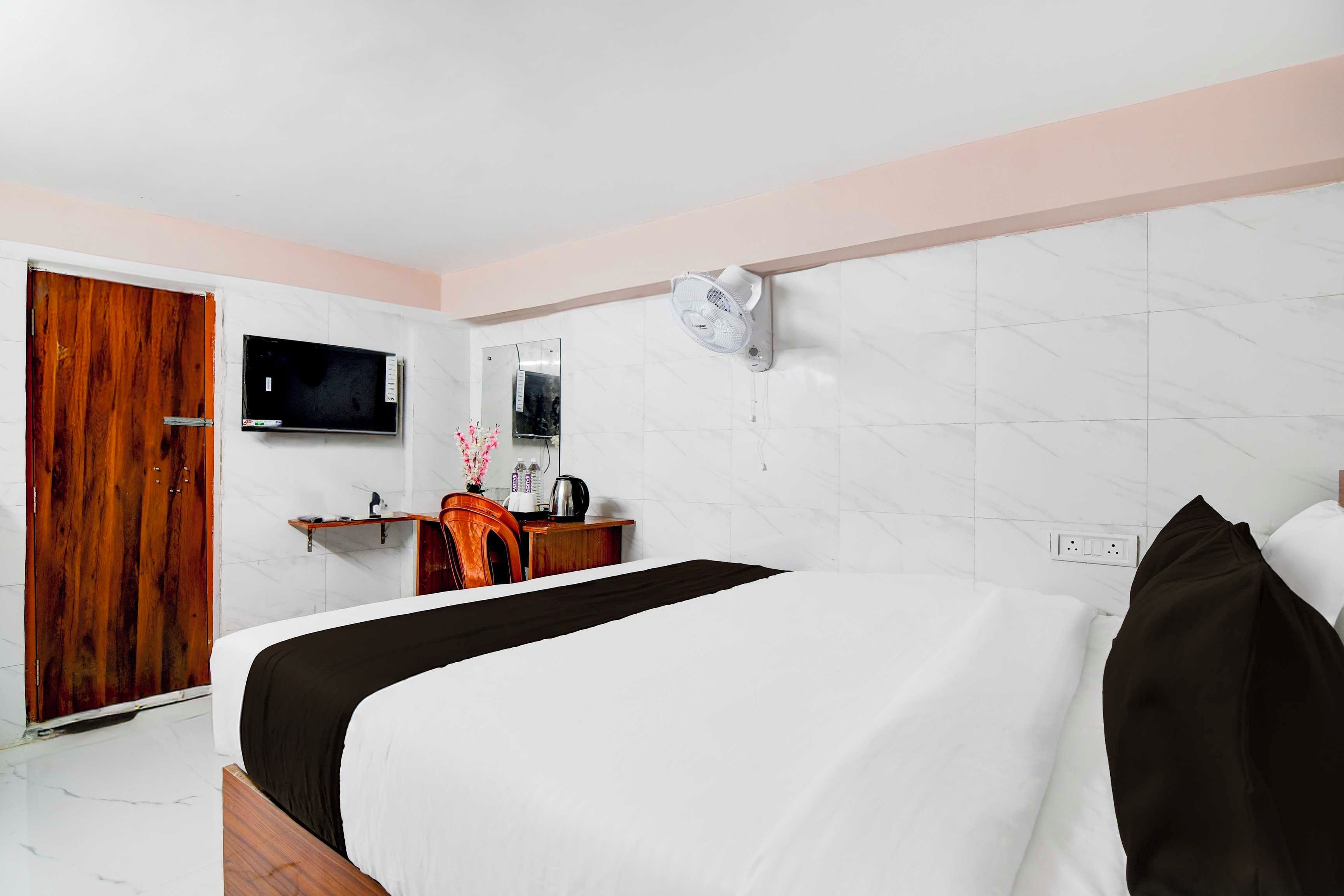 A hotel room with a bed, a wooden wardrobe, a desk with a chair, a television, and a wall-mounted air conditioner.