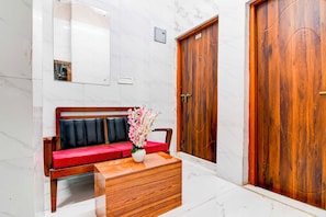 A hotel lobby with a marble floor, a wooden bench with red cushions, a wooden side table with a vase of flowers, and two wooden doors. - Collection O Kolkata Jadavpur University (Bidhannagar)