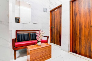 A hotel lobby with a marble floor, a wooden bench with red cushions, a wooden side table with a vase of flowers, and two wooden doors.
