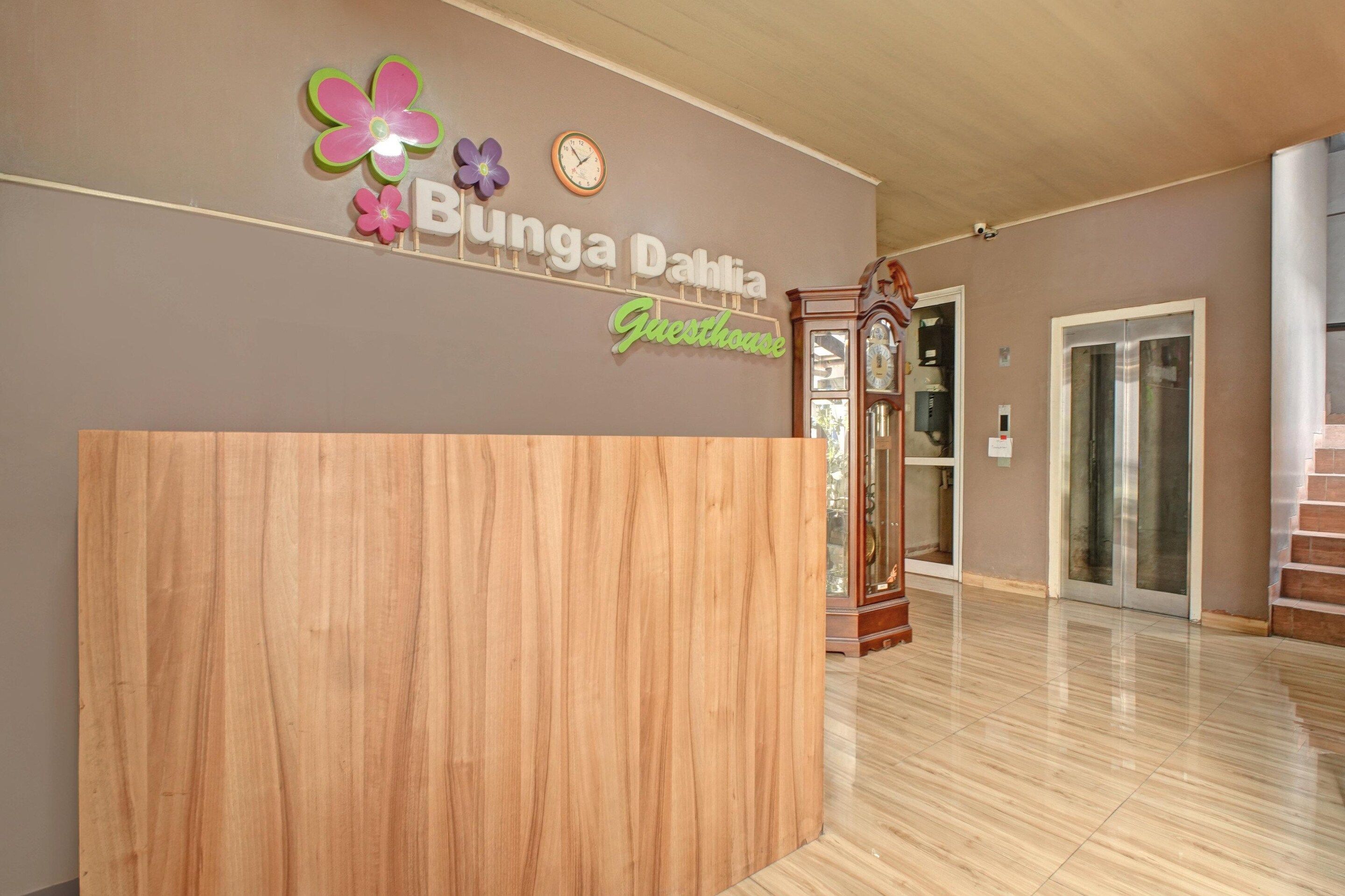A reception desk area with a wooden counter, a wall-mounted clock, and a sign that reads 'Bunga Dahlia Guesthouse.'