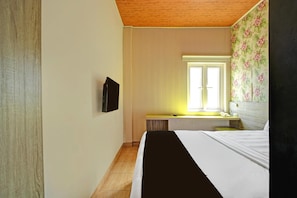 A hotel room with a bed, a television, a window with blinds, a bathroom with a mirror, and a floral wallpaper. - Luxury Deluxe DBL Retreat W/ Free Wifi and Parking (Jakarta)