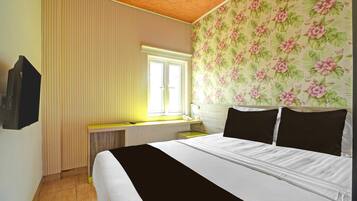 A hotel room with a bed, a window with blinds, a desk with a telephone, and a wall with floral wallpaper.