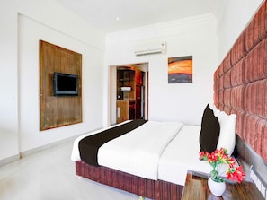 A hotel room with a bed, a flat-screen TV mounted on a wooden panel, a painting on the wall, and a potted plant with flowers. - Townhouse Bharuch Railway Station (Bharuch)