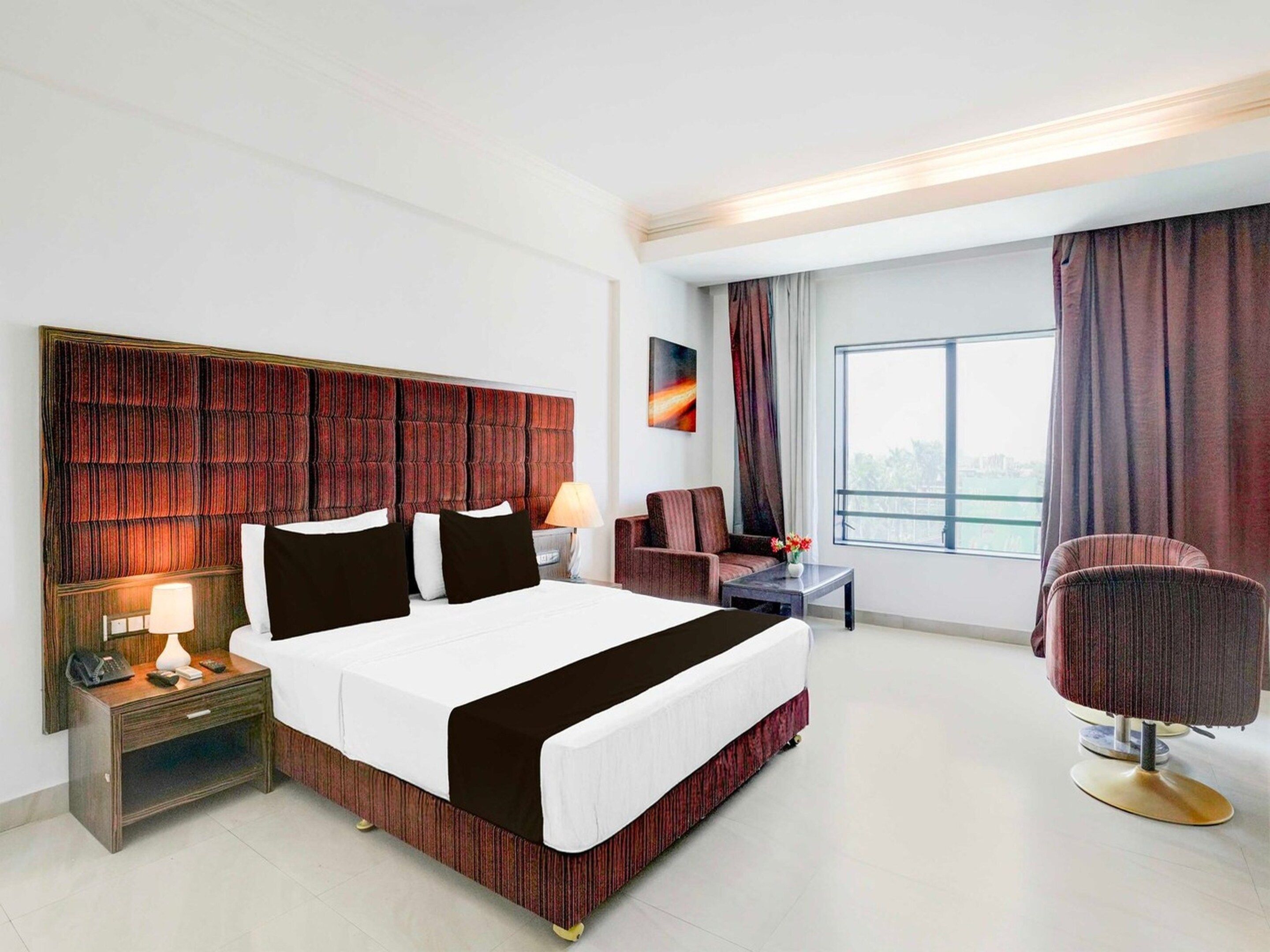 A hotel room with a large bed, a desk, a chair, and a window with curtains.