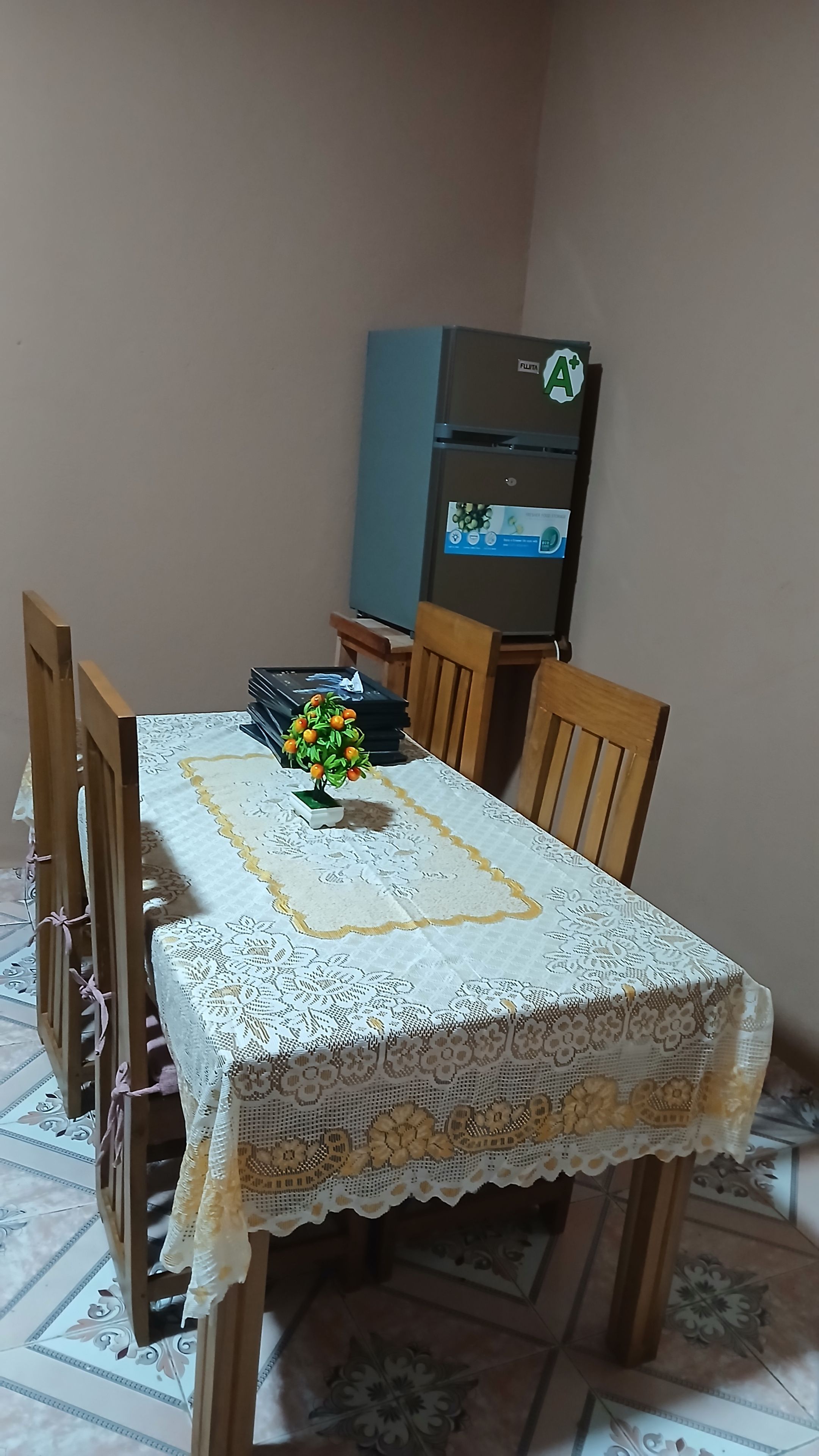 Una mesa de comedor con mantel de encaje, rodeada de sillas de madera y una pequeña planta en maceta con flores amarillas.