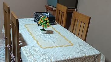 Una mesa de comedor con mantel de encaje, rodeada de sillas de madera y una pequeña planta en maceta con flores amarillas.