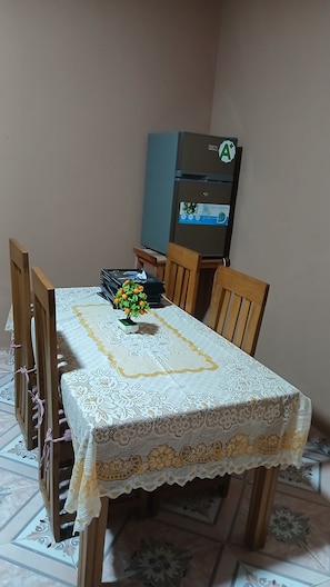 A dining table with a lace tablecloth, surrounded by wooden chairs, and a small potted plant with yellow flowers.