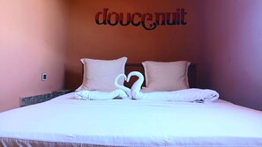 A hotel room with a bed featuring a heart-shaped towel arrangement and a wall with the word 'doucenuit' in a decorative font. - CHAMBRE LA TERRASSE Nosy-Be (Hell-Ville)