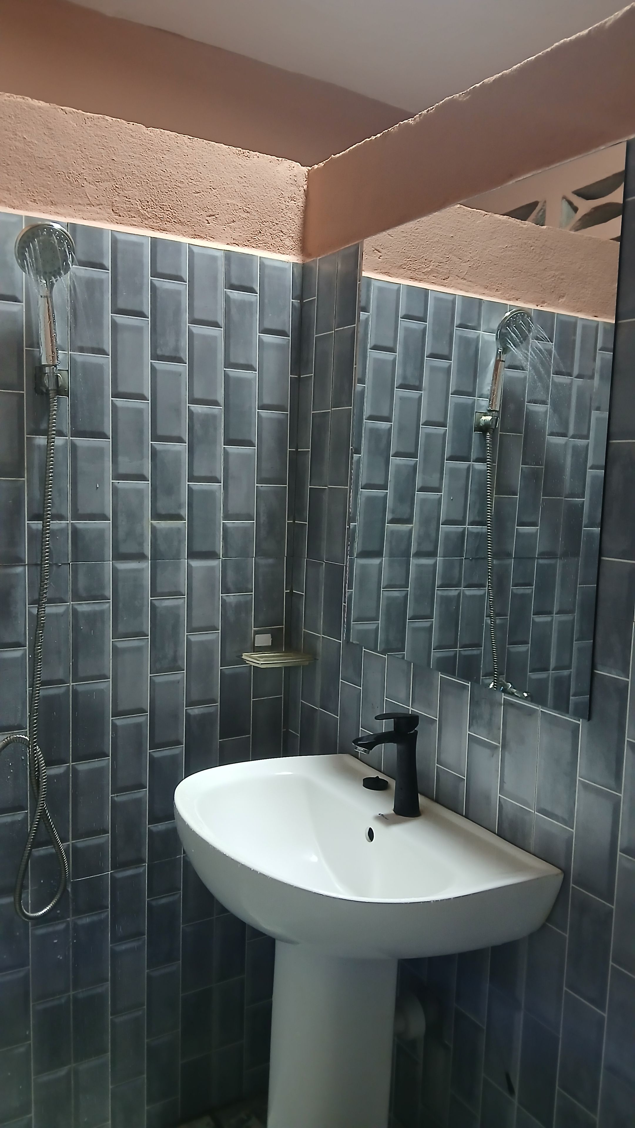 Een badkamer met een wit wastafel, een spiegel en een douche met een handdouche.