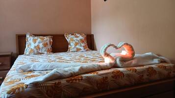 Una cama con colcha de estampado floral, dos almohadas con diseño similar y una disposición de toallas en forma de corazón sobre la cama.