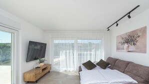 A modern bedroom with a bed, a TV, a sofa, and a window with curtains. - Casa Mia with heated pool (Danilo Biranj)