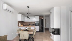 A modern kitchen with white cabinets, a dining area with a wooden table and chairs, and a built-in fireplace. - Casa Mia with heated pool (Danilo Biranj)
