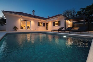 Uma casa moderna com piscina, área de estar externa e entrada bem iluminada.
