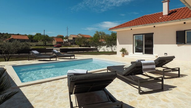 A swimming pool with lounge chairs, a clear sky, and a building with a red-tiled roof. - Casa Mia with heated pool (Danilo Biranj)