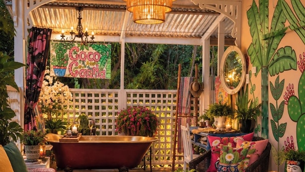 A cozy, well-decorated room with a vintage bathtub, wicker furniture, and lush greenery.