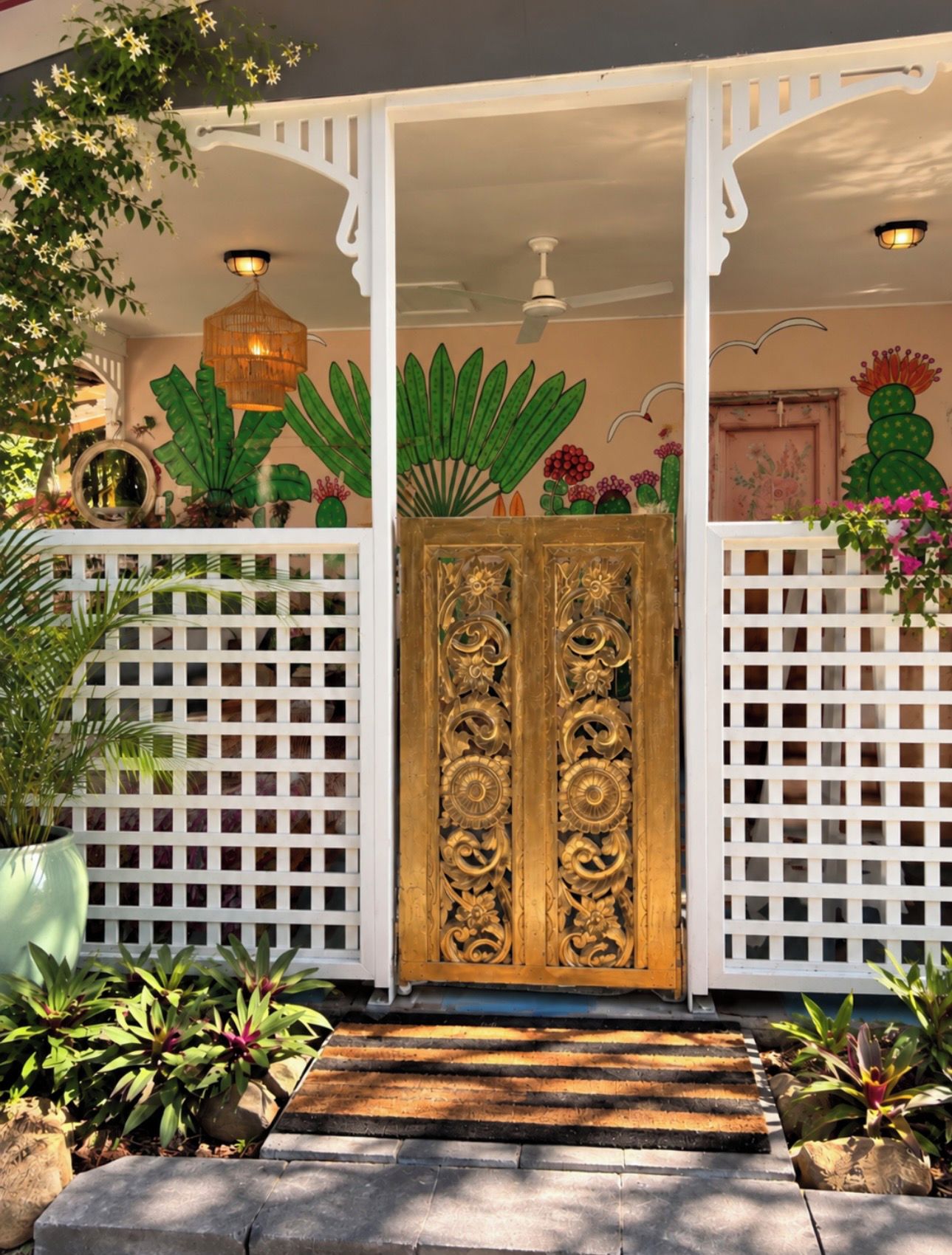 A gated entrance with a decorative golden door, white lattice panels, and a small wooden step leading up to the door.